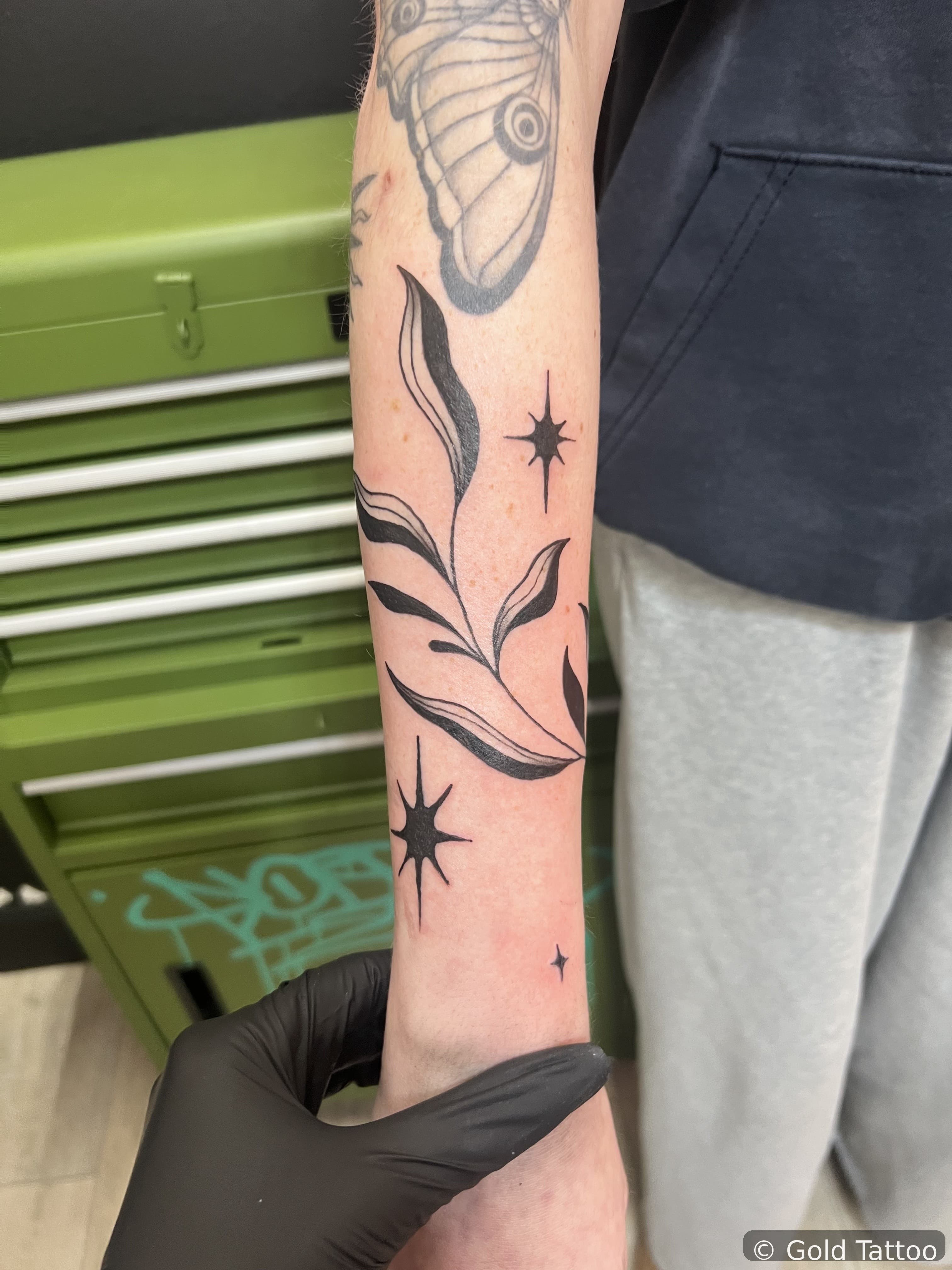 Black fine line leaf vine and stars tattoo on a forearm by Gia “DOC” at Gold Tattoo, 1506 S Las Vegas Blvd, Unit 3