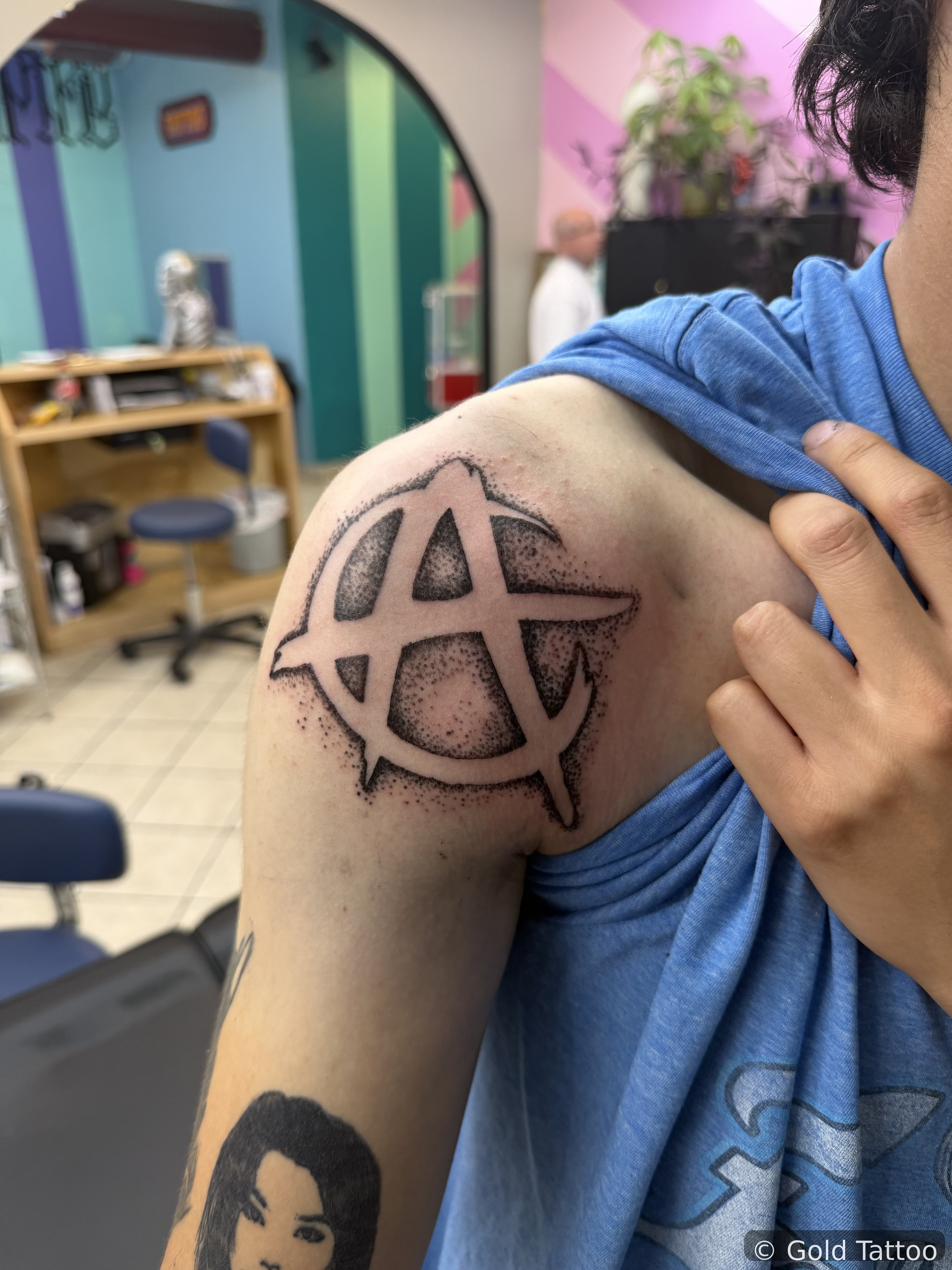 Black dotwork anarchy symbol tattoo on a shoulder by Gia “DOC” at Gold Tattoo, 1506 S Las Vegas Blvd, Unit 3