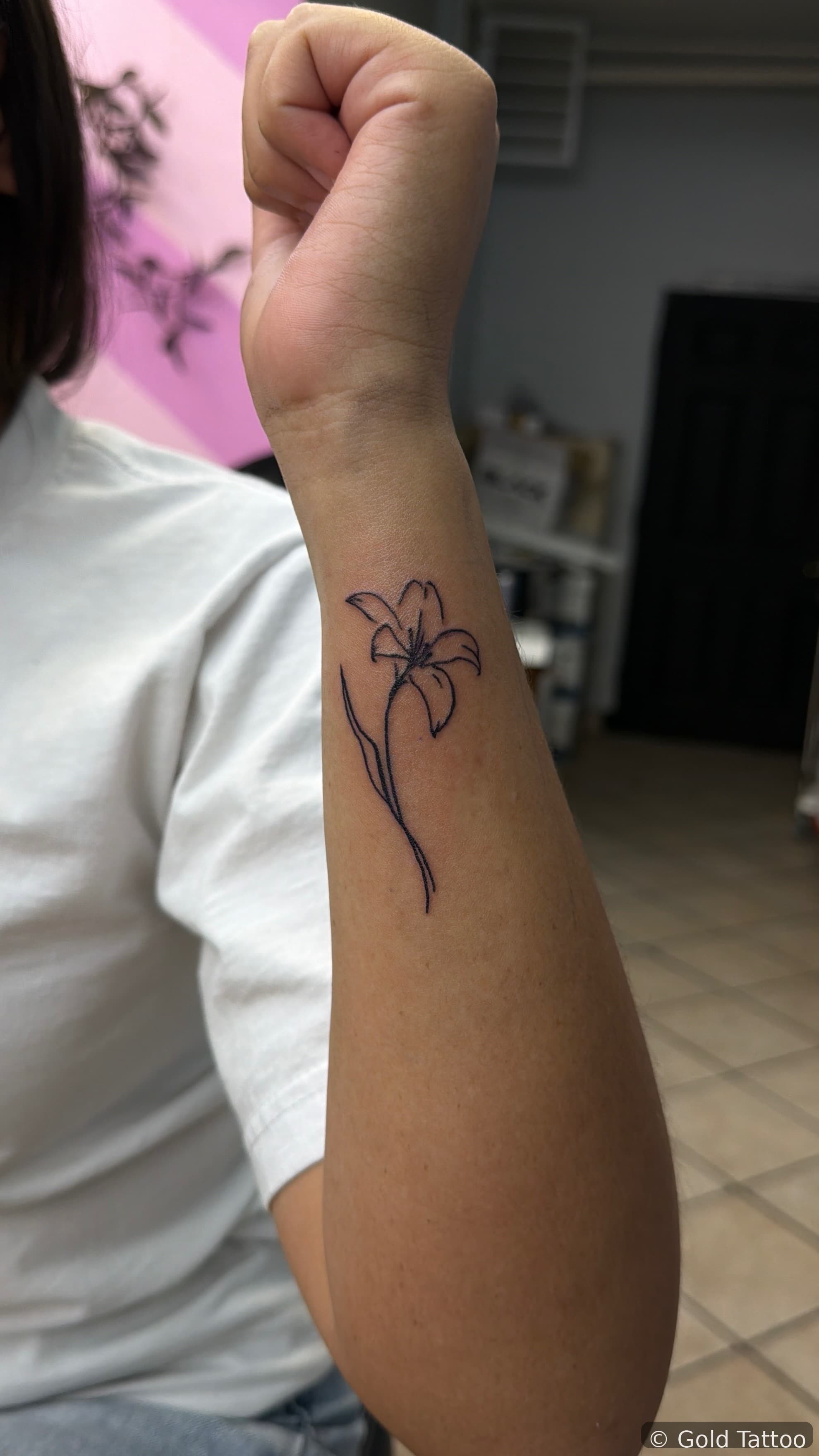 Fine line lily flower tattoo on a forearm by Gia “DOC” at Gold Tattoo, 1506 S Las Vegas Blvd, Unit 3